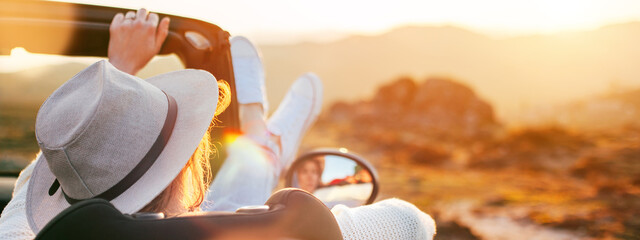 A young woman enjoys a sunset from a convertible