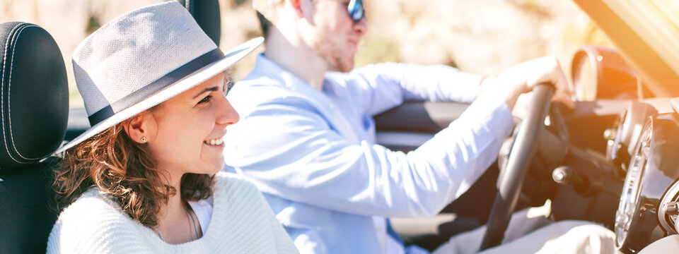 A young couple is riding a convertible and a girl is watching the road on the phone