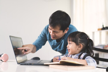 Fototapeta na wymiar Asian father is helping and support daughter to studying the lesson of online class, concept of role of parent to supporting the child homeschooling.