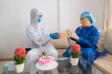 Woman with a protective mask gives her friend a gift on her birthday. Birthday celebration at the time of the pandemic 