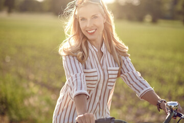 Portrait of a beautiful woman smiling happy while wearing a striped shirt and riding a bicycle in the countryside in a sunny day