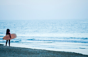 Surfer woman with surfboard looking at the sea on sand at the beach