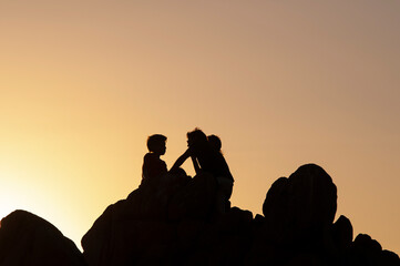 Two friends relax and enjoy nature on top of the rock. Silhouette of people at sunset in the Chilean coast