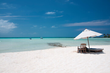 A sunny summer morning on the beautiful white sand beach with a chaise lounge and umbrella on the shore of the Caribbean sea on Isla Mujeres, Mexico