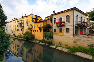 Fototapeta na wymiar Buildings of various eras and architectural styles along the banks of the Retrone river in the city of Vicenza. Some are restored others worn out. Reflections on the water, spring afternoon. Italy.