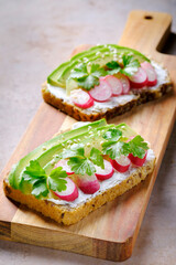 Fresh vegetarian open sandwiches with cream cheese, avocado, radish  and parsley on a wooden cutting board. Concept of healthy eating