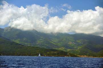 Sailing yacht near the Italian coast with mountains that covered thick vegetation