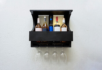 Five bottles and four glass of elite wine on wooden shelf.