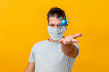 A man with a yellow background and his face covered by a medical mask holds a coronavirus or covid19 conceptually with his hand