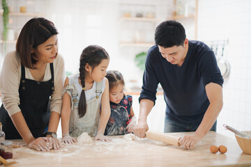 Obraz na płótnie Canvas Young Asian love family are preparing the dough powder, cookies, cake on table in the kitchen which Excited smiling and felling happy. parent and daughter are cooking on the day at home.
