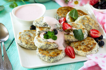 Summer breakfast close-up. Homemade cottage cheese pancakes with poppy seeds, sour cream sauce with strawberries.