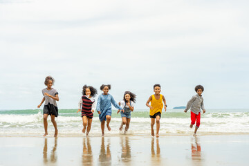 group of children sister brother run and play happily together on the beach during the summer while visiting with family or school.
