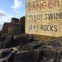Danger sign in Ireland, do not swim near rocks blue sky beach