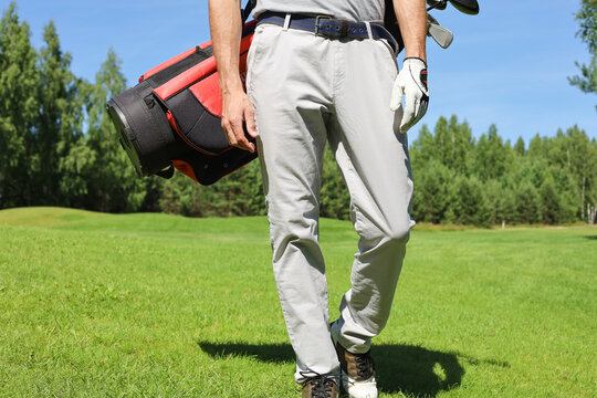 Cropped image of male golfer carrying golf bag with drivers while walking by green grass.