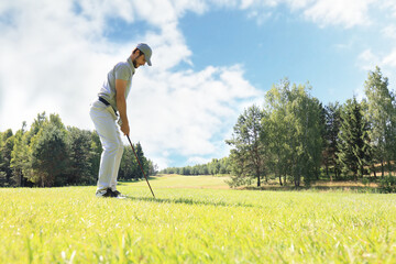 Full length of golf player playing golf on sunny day. Professional male golfer taking shot on golf course.