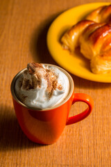 Cup of frothy cappuccino next to some croissants. Selective focus.