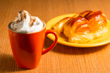 Cup of frothy cappuccino next to some croissants. Selective focus.