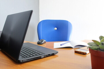 Office workplace interior with laptop notebook mouse notebook phone pen flower in a pot on the table. Empty workplace with wooden table and blue chair