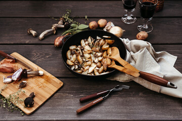 Roast forest mushrooms, potatoes, onions and seasonal herbs in a cast iron pan and ingredients on a wooden background outdoors.