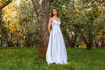 Obraz na płótnie Canvas Bride in white dress is standing by the tree