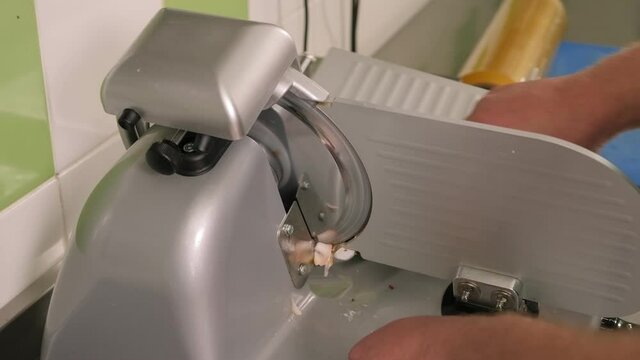 Slicing machine slice cheese. Chef using ham slicer machine. Slicing bacon. Close-up of the chef slicing ham or bacon in the restaurant kitchen. Slow motion.