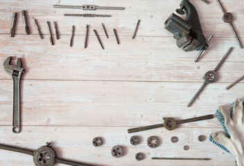 Old equipment for manual cutting of external and internal threads. Locksmith vises, dies and taps of different diameters, a pipe wrench and work gloves on a wooden background. Free space.