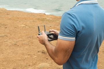 Young Man watching and navigating a flying drone near the ocean