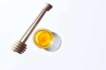 Honey in a small glass plate on a white background. Nearby lies a wooden spoon
