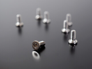 Fototapeta premium A group of white bolts on a dark matte surface. One of them lies, the others stand. Illustration of small light screws close-up. Assembly and repair of electronic equipment and computer hardware
