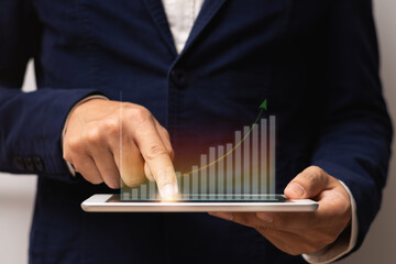 Businessman holding tablet and use he finger touch on screen with virtual hologram growth graph chart and arrow up.