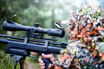 Hunter in camouflage uniform aim with gas air rifle. Soldier ifles with telescopic sight