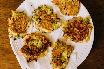 Pan Fried Vegetable Fritters Served on a White Plate on a Wood Table. These fritters are made with mixed vegetables, egg, and flour. Horizontal Photo.