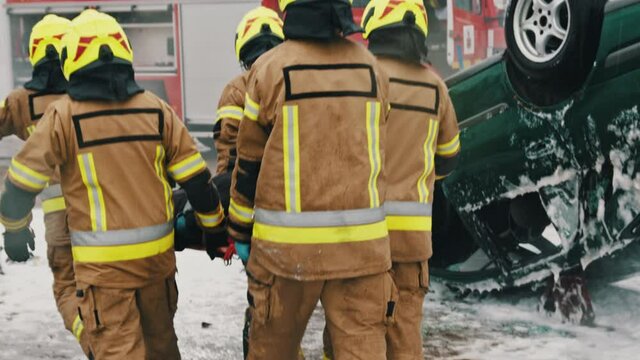 Firefighters rescuing injured person after the car accident. Slow motion.