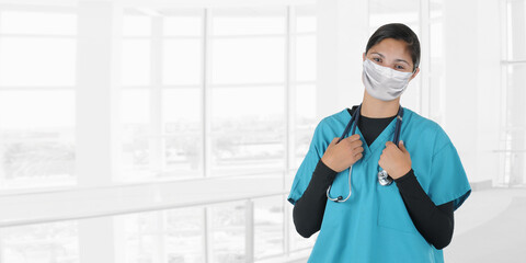 Fototapeta na wymiar Young woman nurse or doctor holding stethoscope draped around her neck with a blurry modern medical facility background, with copy space.