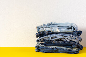 A stack of different jeans trousers close up on yellow and white background, casual clothes