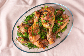 Baked chicken drumsticks with rosemary, spices, onions and dill on a pink tablecloth, top view