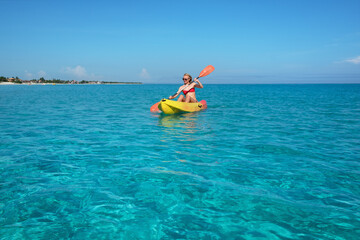 girl paddles a kayak in the turquoise waters