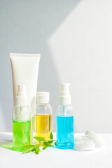 Gel green and blue, yellow oil for face care in glass bottles. Jar of cream and a white tube. leaves and flowers. Vertical photo