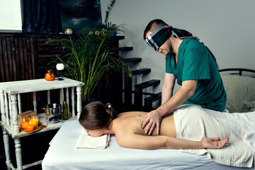 Masseur with blindfold doing blind massage of a young woman. Beautiful relaxed face of a young woman with brown hair and closed eyes.