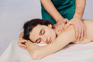 Fototapeta na wymiar The hands of a male masseur doing massage of a young woman. Beautiful relaxed face of a young woman 27 years old with brown hair and closed eyes on a blue background.