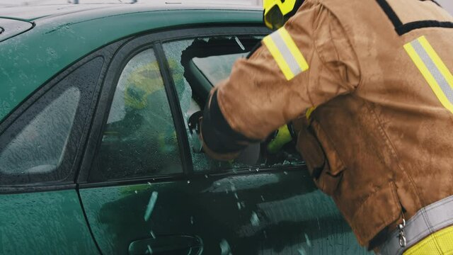 Car accident rescue, firefighter breaking the glass on the car and checking for the injured people. Close up, Slow motion shot.