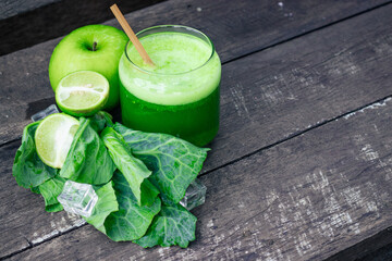Green apple smoothie in glass and kale leaves on wooden table