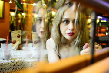 European blonde girl in elegant blue clothes is sitting in a cafe with a cocktail.