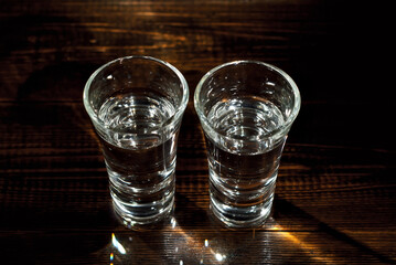 Glasses with alcohol close up. Vodka on a brown wooden background. Glass table from worn shabby boards.