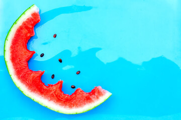 Summer creative watermelon layout. Bitten slice of fresh jucy watermelon with some seeds on light blue background. International watermelon day. Copy space