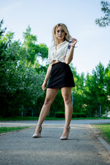 A teenage girl in a black skirt and white blouse. Light, elegant hair. Sunglasses. It stands in a Park on an asphalt path.