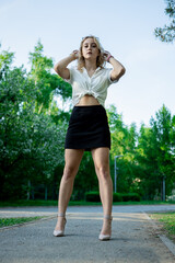 A teenage girl in a black skirt and white blouse. Light, elegant hair. Sunglasses. It stands in a Park on an asphalt path.