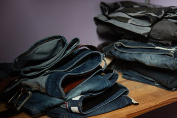 Closeup of a stack of folded navy jeans on a wooden shelf. Denim, levis. leather belt with metal buckle