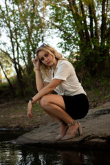 Girl near the water. A blonde woman in a white shirt poses on the Bank of a river or lake.