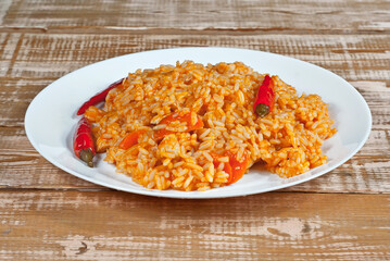 Pilaf with meat, peppers and carrots in a white plate. Rice on a wooden pink board.